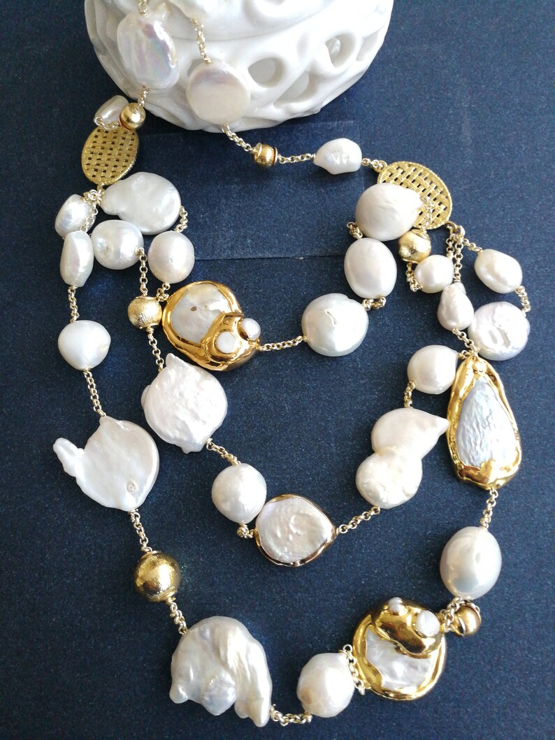 May include: A multi-strand necklace with large white baroque pearls and gold accents. The necklace features a variety of pearl shapes and sizes, including round, oval, and irregular.