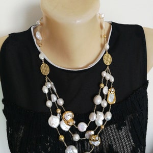 May include: A multi-strand necklace with large white pearls and gold accents. The necklace features a variety of pearl shapes, including round and oval. The gold accents include small beads and larger, decorative pieces.