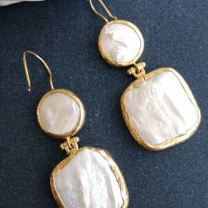 May include: A pair of gold tone earrings with white baroque pearl drops. The earrings feature a round pearl drop and a square pearl drop.