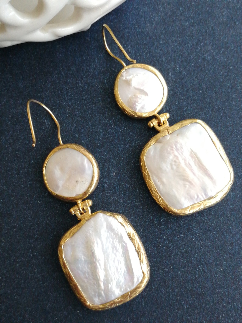 May include: A pair of gold tone earrings with white baroque pearl drops. The earrings feature a round pearl drop and a square pearl drop.
