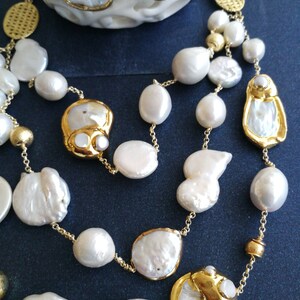 May include: A gold chain necklace with white pearl beads and gold accents. The necklace features large, irregular shaped pearls.