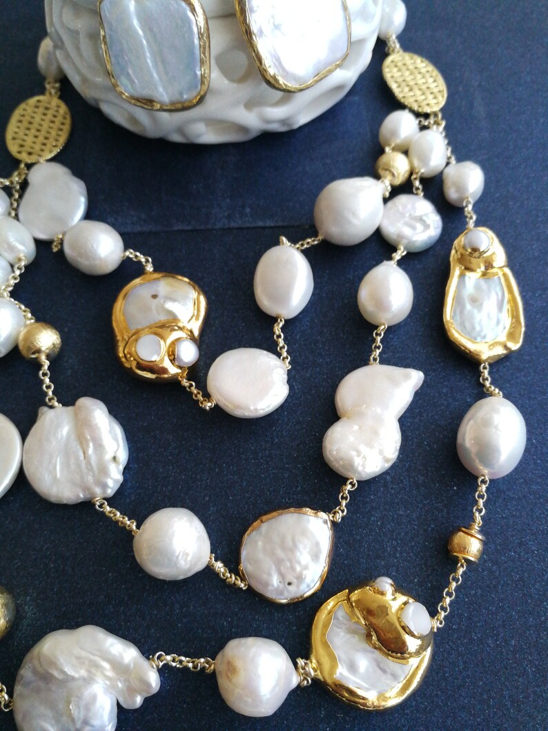 May include: A gold chain necklace with white pearl beads and gold accents. The necklace features large, irregular shaped pearls.