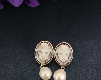 May include: A pair of gold earrings with a white cameo of a lion's head and a pearl drop.