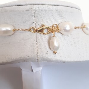 May include: A gold chain necklace with white pearl beads. The necklace has a lobster clasp closure and a single pearl drop pendant.