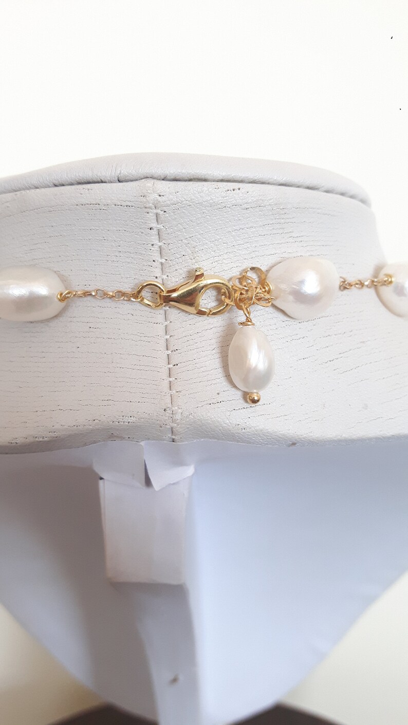 May include: A gold chain necklace with white pearl beads. The necklace has a lobster clasp closure and a single pearl drop pendant.