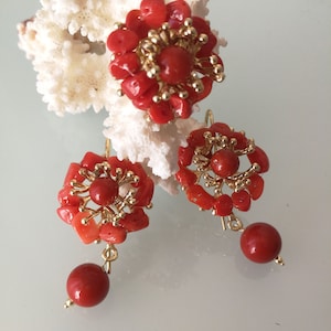 May include: A set of coral earrings and a ring. The jewelry is made of red coral and gold. The earrings have a flower design with a single red coral bead dangling from each earring.