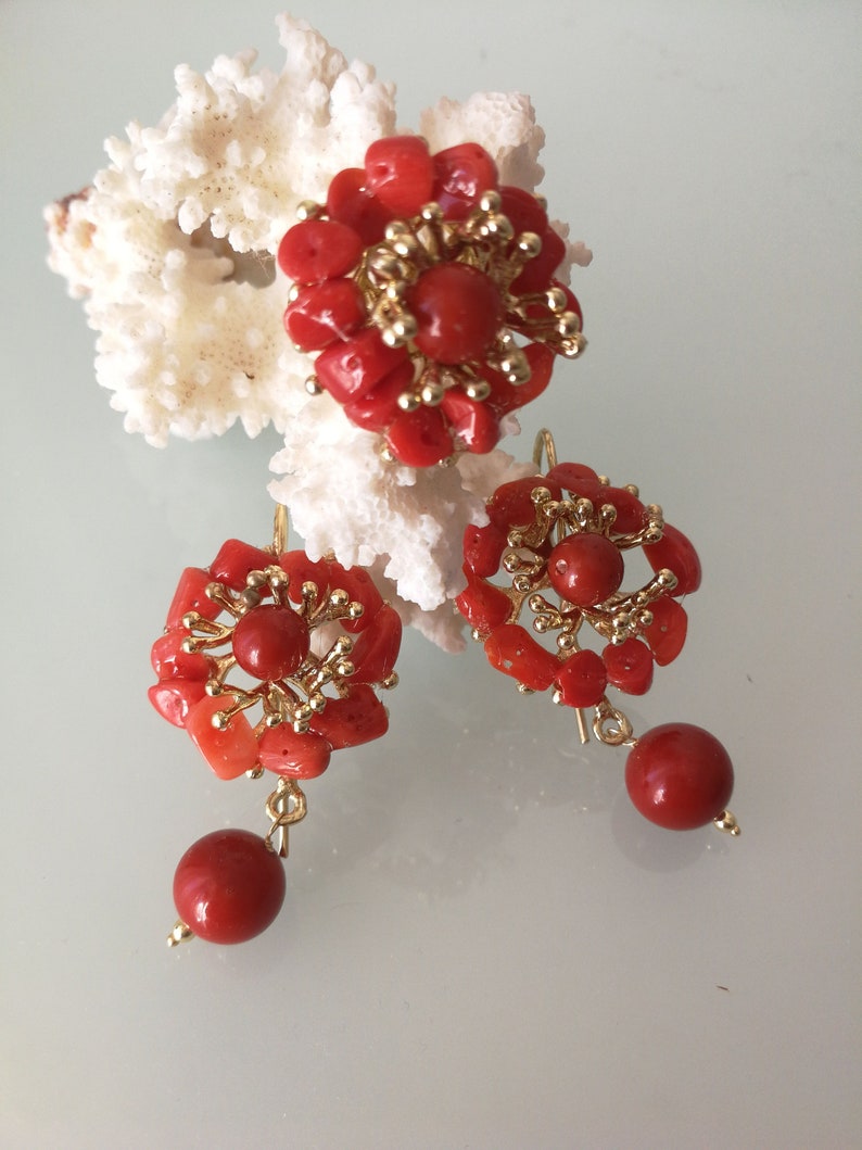 May include: A set of coral earrings and a ring. The jewelry is made of red coral and gold. The earrings have a flower design with a single red coral bead dangling from each earring.