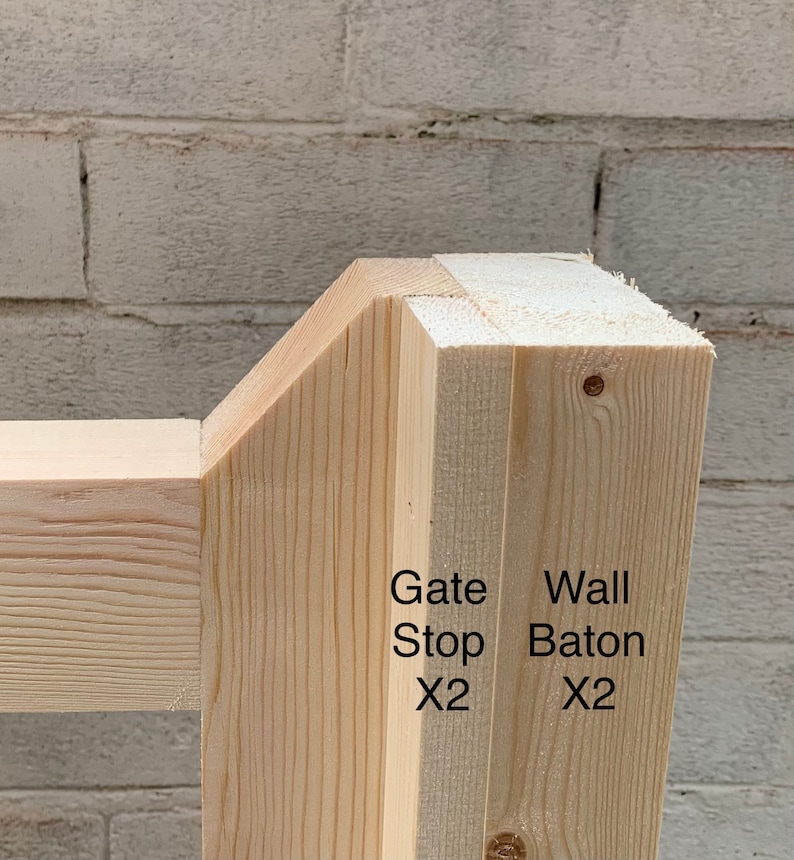 May include: Close-up of a wooden gate stop and wall baton, both made of unfinished wood. The gate stop is labelled "Gate Stop x2" and the wall baton is labelled "Wall Baton x2".