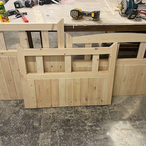 May include: Three unfinished wooden gate panels with a slatted design and a decorative top rail. The panels are arranged on a light wood surface.