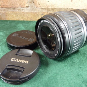 May include: A black Canon EF 75-300mm f/4-5.6 III lens with a silver barrel and a black lens cap. The lens is on a green surface.