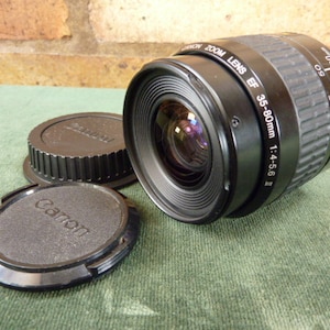May include: A black Canon EF 35-80mm 1:4-5.6 II zoom lens with a black lens cap and a black lens hood.