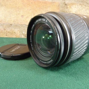 May include: A black Konica Minolta AF 35-120mm 1:3.5-5.6 D zoom lens with a silver lens barrel and a black lens cap.