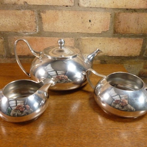 May include: A silver teapot, creamer, and sugar bowl set. The pieces are all shiny and reflect the surrounding environment.