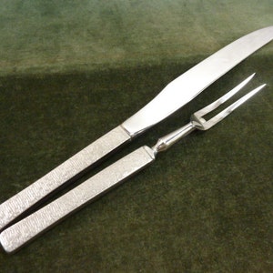 May include: A silver carving set with a knife and fork. The handles of both utensils have a textured finish.