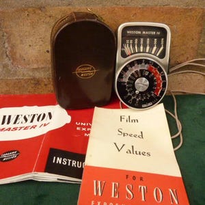 May include: A vintage Weston Master IV light meter with a silver face and black markings. The meter is in a brown leather case and comes with instructions for use. The instructions include a chart for film speed values.