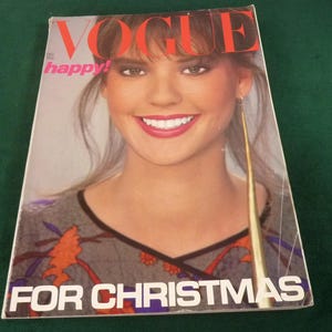 Peut inclure: Une couverture de magazine Vogue de décembre 1980 montrant une personne souriante aux cheveux bruns. Le texte VOGUE apparaît en grandes lettres rouges en haut, avec happy! en rose et FOR CHRISTMAS en blanc en bas. La personne porte un haut gris à motifs.