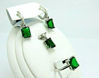 May include: A set of emerald green gemstone jewelry featuring a ring, a pendant, and a pair of earrings. The jewelry is made of silver and features square-shaped gemstones.