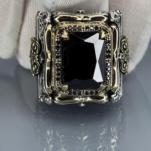 Gloved close-up front view of the square black onyx stone set in an ornate 925 sterling silver Ottoman-style bezel on gray background.