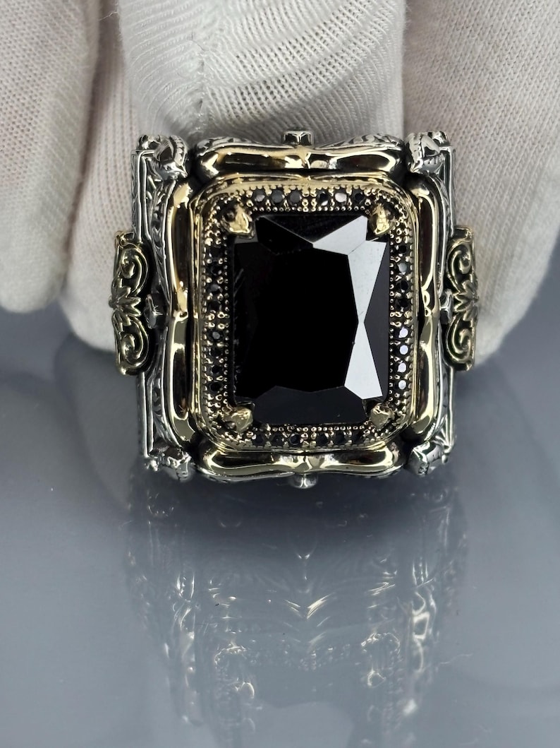 Gloved close-up front view of the square black onyx stone set in an ornate 925 sterling silver Ottoman-style bezel on gray background.