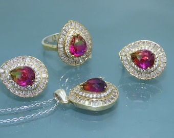 Puede incluir: Un conjunto de joyas con una piedra preciosa roja en forma de pera rodeada por un halo de piedras blancas más pequeñas. El conjunto incluye un anillo, un collar y un par de pendientes.