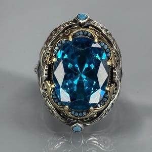 Straight-on close-up on gray background of the aquamarine gemstone ring with decorative border and 925 sterling silver setting.
