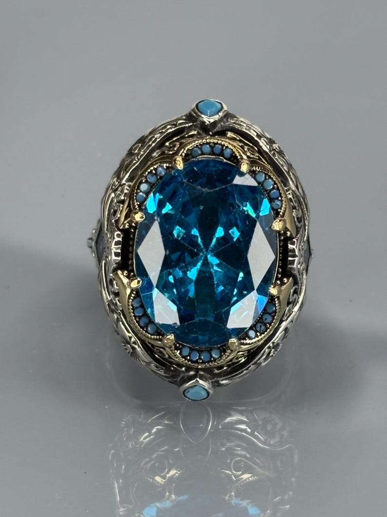Straight-on close-up on gray background of the aquamarine gemstone ring with decorative border and 925 sterling silver setting.