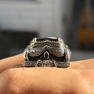 On-hand angled close-up showing the raised black onyx stone and ornate 925 sterling silver band details.