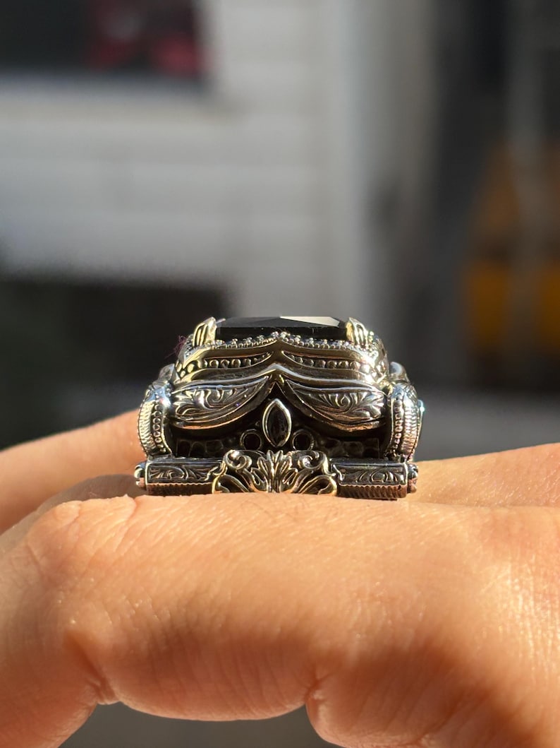 On-hand angled close-up showing the raised black onyx stone and ornate 925 sterling silver band details.