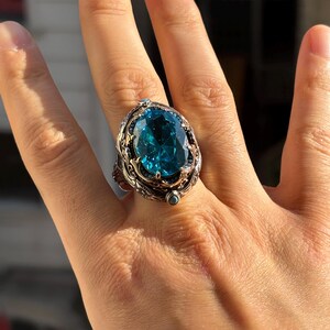 On-hand photo from a slightly wider view showing the oval aquamarine stone ring worn on finger in natural light.