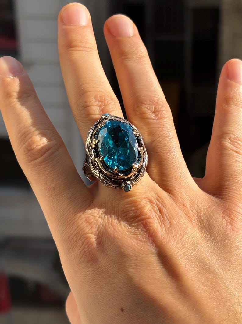 On-hand photo from a slightly wider view showing the oval aquamarine stone ring worn on finger in natural light.