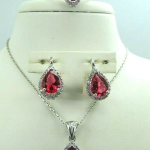 May include: A silver necklace, ring, and earrings set with a pear-shaped red gemstone surrounded by smaller clear gemstones.