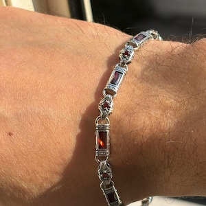 May include: Silver bracelet featuring rectangular and round red gemstones. The bracelet has an ornate design with detailed metalwork. The gemstones are set in a silver link chain, creating a classic and elegant look. A piece of jewelry.
