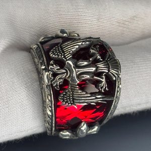 This image captures the radiant shine of the ruby under direct lighting. The vivid red hues reflect through the expertly cut facets of the gemstone. The bold color contrasts beautifully with the textured sterling silver base.