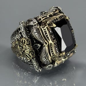 Three-quarter product shot on gray background showing the ring’s chunky build, carved patterns, and black onyx stone depth.