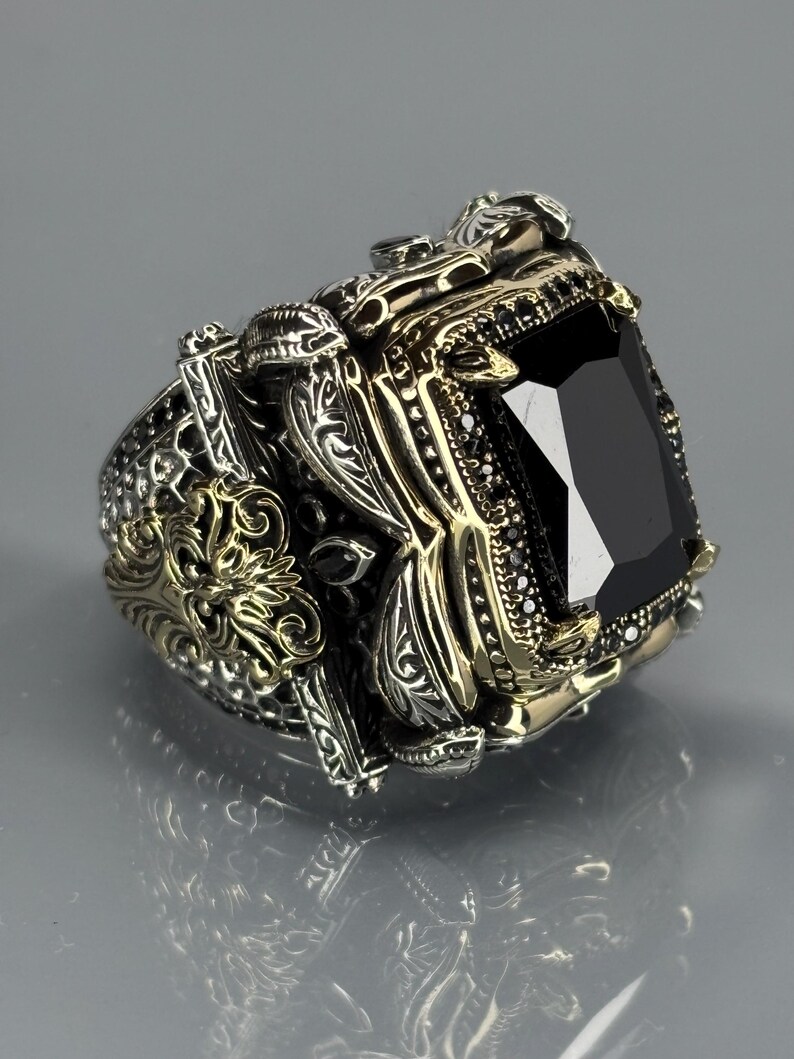 Three-quarter product shot on gray background showing the ring’s chunky build, carved patterns, and black onyx stone depth.