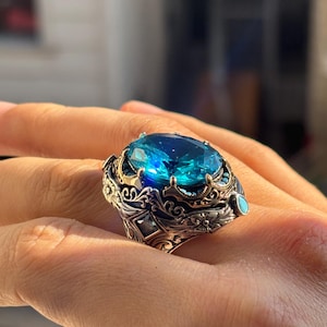 On-hand close-up focusing on the aquamarine stone’s blue shine and the ring’s layered, engraved top design.