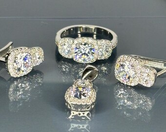 Könnte beinhalten: Eine Sammlung von silberfarbenem Schmuck mit funkelnden Zirkonia-Steinen. Das Set umfasst einen Ring, einen Anhänger und ein Paar Ohrringe, alle mit einem Halo-Design. Der Ring und die Ohrringe haben drei Steine, während der Anhänger einen hat.