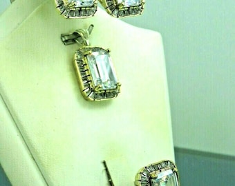 Könnte beinhalten: Ein Goldschmuck-Set mit einem Ring, einem Anhänger und Ohrringen. Jedes Stück verfügt über einen großen, klaren, smaragdgeschliffenen Stein, der von kleineren Steinen umgeben ist.