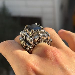 On-hand three-quarter view showing the bold square black onyx centerpiece and engraved shoulders of the Turkish silver ring.
