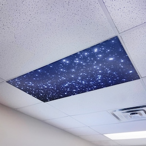 May include: A white ceiling with a blue and white star-shaped ceiling tile. The tile is lit up with white lights, creating a starry night effect.
