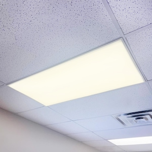 May include: A rectangular, recessed fluorescent light fixture installed in a drop ceiling. The light emits a bright, even glow, contrasting with the textured, white ceiling tiles. The metal frame of the light fixture is silver.
