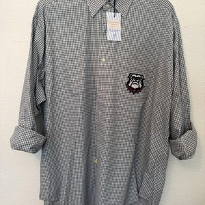 May include: A long-sleeve button-down shirt with a black and white micro-check pattern. The shirt features a collar, a front button placket, and a patch on the chest depicting a bulldog with a red collar. A white tag with text is attached.