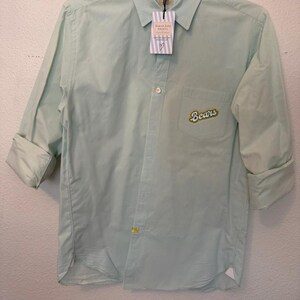 May include: A light mint green button-down shirt with long sleeves rolled up to the elbows. The shirt features a chest pocket with an embroidered patch that reads "Bears" in yellow and white text. A branded tag hangs from the collar.
