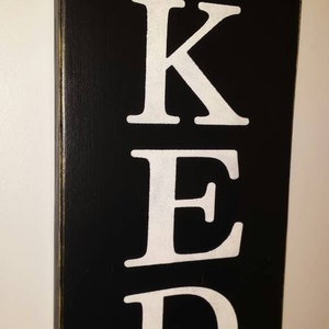 May include: Black wooden sign with the word "BAKED" written in white letters.