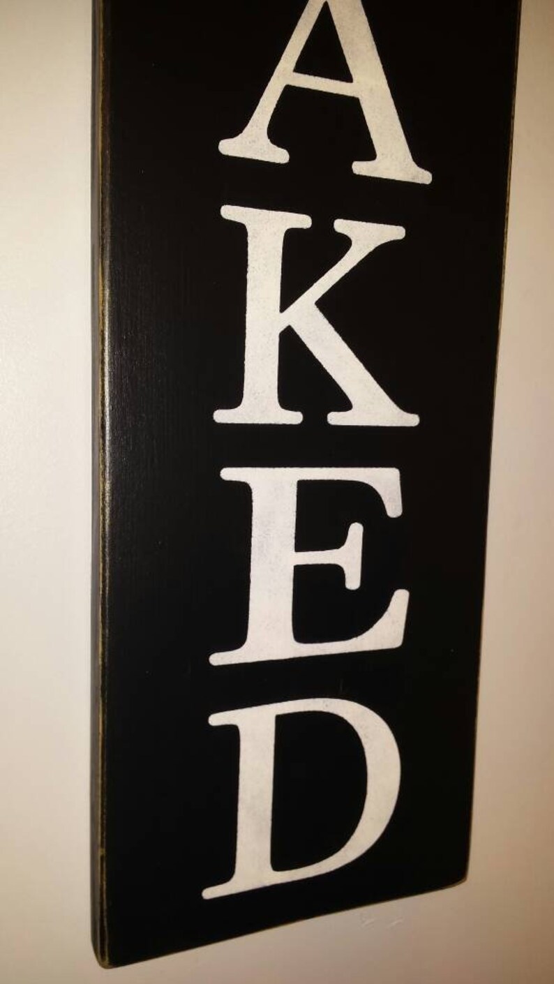 May include: Black wooden sign with the word "BAKED" written in white letters.