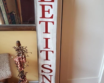 Puede incluir: Un letrero de madera blanco con letras rojas que dice "Let It Snow". El letrero está desgastado y tiene un aspecto rústico.