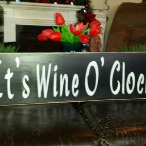 Könnte beinhalten: Schwarzes Holzschild mit weißer Aufschrift "It's Wine O'Clock".