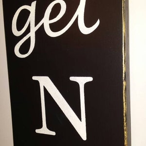 May include: Black wooden sign with white painted text that reads "get N A".