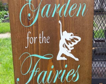 May include: A wooden sign with the text "Leave room in the garden for the fairies to dance" in white and teal lettering. A white silhouette of a fairy is in the center of the sign.