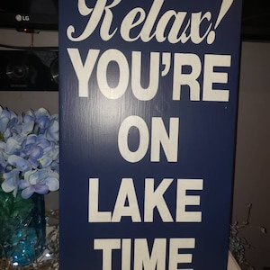 Puede incluir: Un letrero de madera azul con letras blancas que dice "Relax! You're on Lake Time".